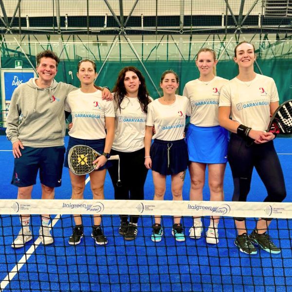 Sei donne si trovano fianco a fianco su un campo da padel al coperto e posano per una foto di gruppo dietro la rete. Quattro indossano magliette bianche abbinate con il logo "Studio dentistico a Busto Arsizio"; una tiene in mano una racchetta, sorridendo con sicurezza.